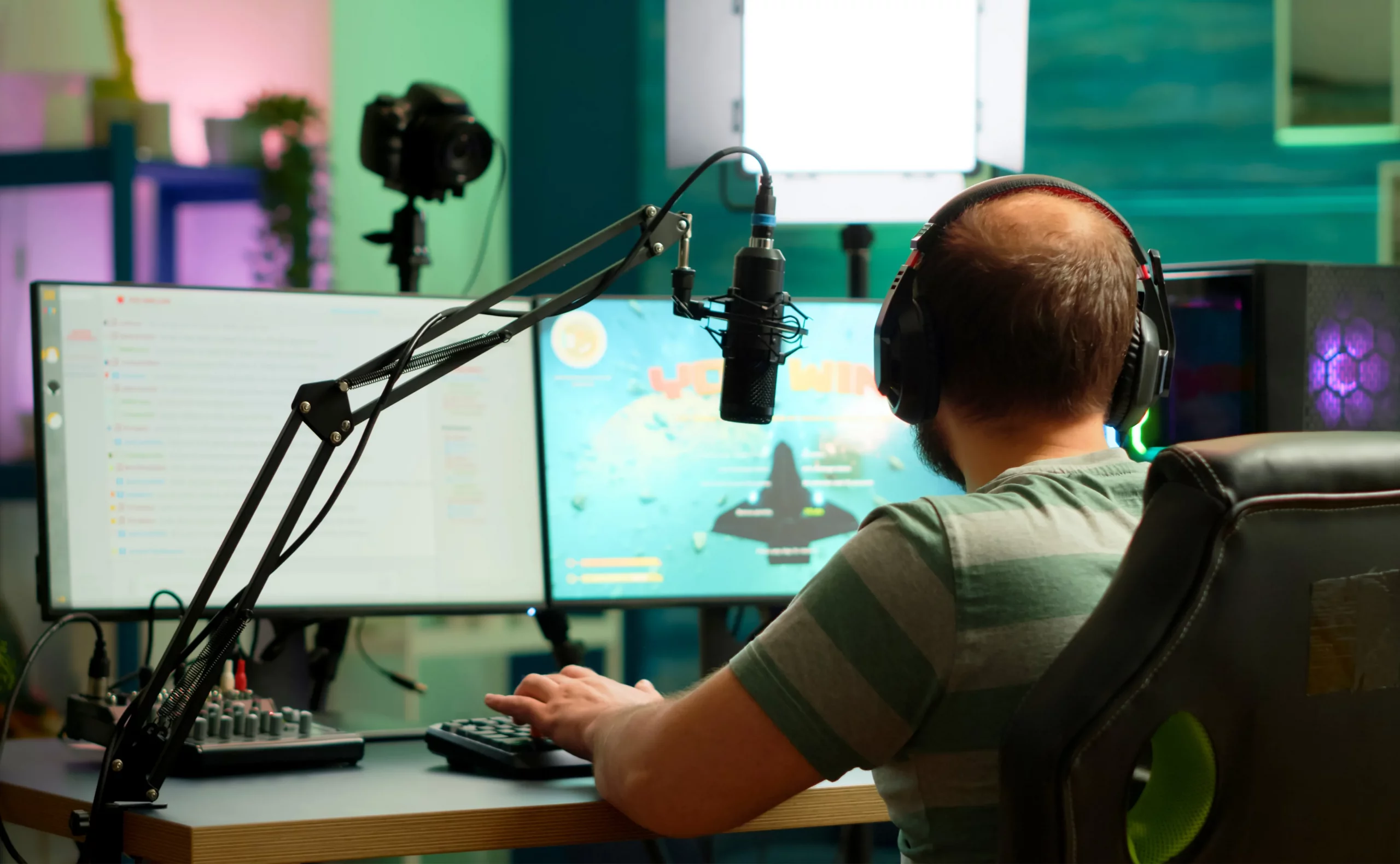 A man wearing headphones sits at a desk in a streaming production studio, focused on his work.