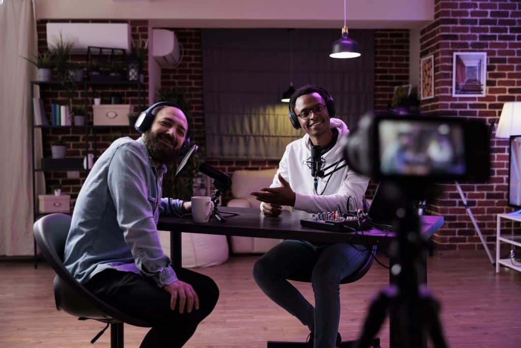 Two men in a podcast studio, seated at a table with a camera and microphone ready for recording.